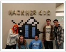 Group of students standing below wall art reading "HACKHER"